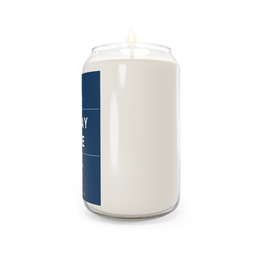 Soy candle in clear glass jar with blue label stripe and lit wick flame visible