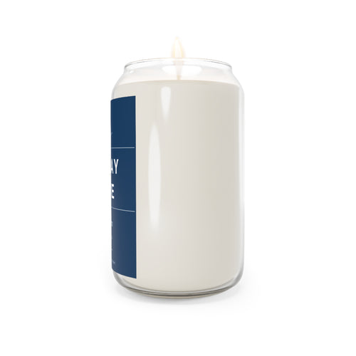 Soy candle in clear glass jar with blue label stripe and lit wick flame visible