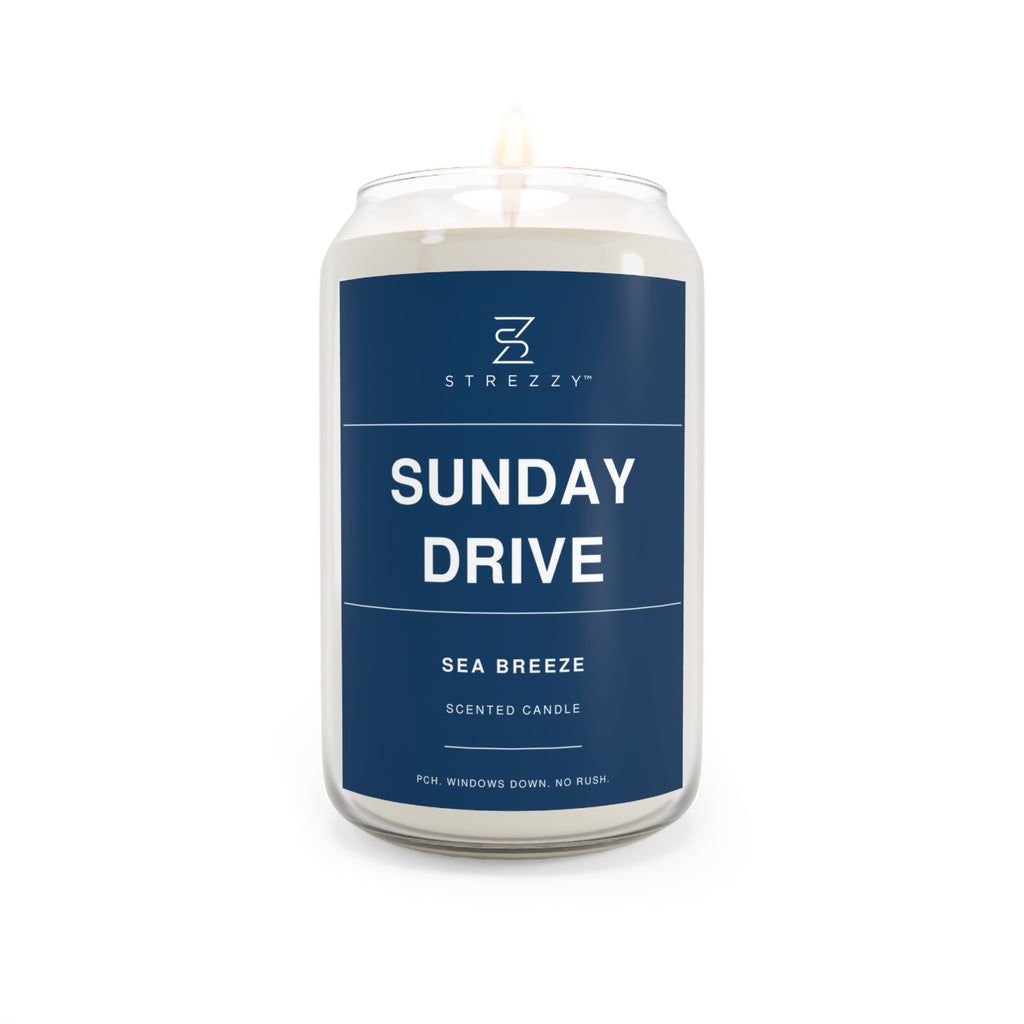 Soy candle in clear glass jar with blue Sunday Drive label and lit wick flame